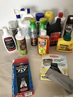 Photo of assorted cleaning and pest control products, including spray bottles and liquid containers arranged on a wooden floor.