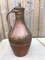 Side view of copper vase showing its bulbous shape, handle, and lid