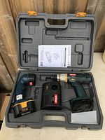 Ryobi cordless drill set with drill, battery pack, charger, auxiliary handle, and manual in gray plastic carrying case, laid open on surface.