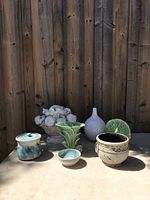 Front view of the six assorted pottery and ceramic items placed on a wooden surface with a wooden fence background.