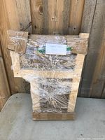 Wooden step stool wrapped in plastic with label, leaning against wooden fence.