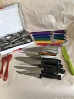 Wide view showing all cutlery including knives, cutlery box with spoons and forks, plastic kitchen brushes and green utensil.