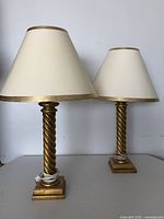 Two decorative table lamps with gold spiral bases and matching cream lampshades with gold trim, showing size difference between them.