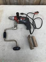 Photo of electric impact drill, hand crank attachment, and wooden jig placed on a table