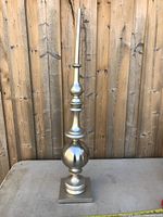 Full view of the tall metal decorative finial with geometric shapes on a square base in front of wooden fencing.