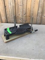 Black and metal miter saw base on a wooden plank, with two upright metal bars and angle markings.