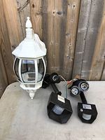 Photo shows white metal and glass outdoor lantern-style lamp with infrared sensor lights placed on table against wood fence background.
