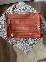 Photo showing the brown leather purse with three horizontal zippered compartments on one side, tassel zipper pulls.