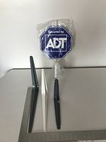 Three metal shelf brackets in dark gray and white colors arranged on a table with small ADT security sign behind them.