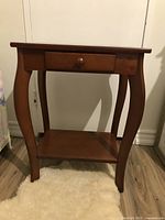 Side view of wooden side table showing curved legs, drawer and bottom shelf