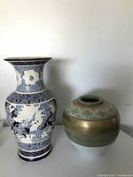 Full view of two vases: a taller blue and white hand painted vase with dragon motifs and a shorter round ceramic vase with gold and floral decorations.