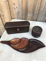 Jewelry box, carved container, and leaf-shaped wooden tray displayed on a table with wood fence background.