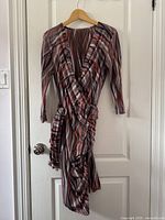 Photo of the multi-color striped wrap dress hanging on a wooden hanger against a white door.