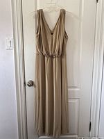 Front view of beige sleeveless long dress by Jones New York hanging on white hanger against white door.