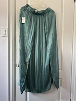 Front view of greenish-blue long skirt with side slit hanging on door, new with tag.