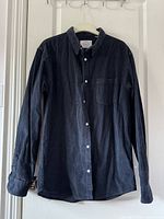 Dark blue velvet long sleeve shirt hanging on hanger, showcasing button-down collar and chest pocket