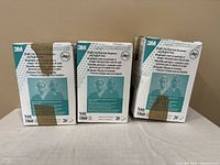 Three sealed boxes of 3M N95 1860 masks on a beige surface, showing condition of boxes and product packaging.