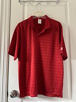 Red Adidas short sleeve polo shirt hanging on door showing front and collar detail