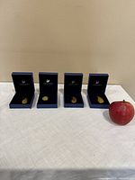 Four Swarovski pendants displayed in blue boxes with an apple for size reference on a white tablecloth.
