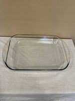 Clear rectangular glass baking dish with handles placed on a white cloth surface. Shows the top view of the empty dish.