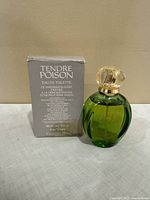 Green glass bottle of Christian Dior Tendre Poison Eau de Toilette next to its original grey demonstration box.