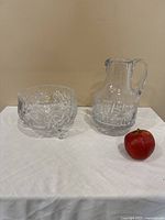 Crystal bowl and crystal pitcher set displayed on white cloth with apple for scale, showing clear glass intricate cut-glass patterns and no chips.