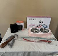 Photo of all dog supplies including dual dog bowls, black muzzle, chain leash, two collars, and apple on table.