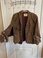 Front side of the brown fur swing coat hung on a hanger showing texture details and faux fur cuffs.