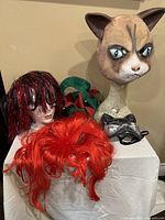 Wide view showing all costume accessories including cat head mask, wigs, jester hat and cat eye mask displayed on foam mannequin heads.