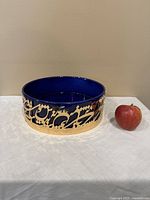 Front view of large blue glass bowl with gold calligraphy design, next to an apple for size reference.