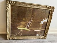 Front view of framed artwork showing large tree and pond landscape under glass with decorative gold-tone carved frame.