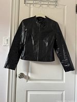 Black genuine leather jacket hanging on a door, front view zipped up.