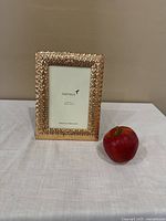 Front view of the gold-tone Papyrus picture frame with textured pattern, showing the frame size and design relative to an apple.