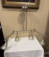 Stainless steel ceiling light fixture with four frosted glass lamp shades placed on table against a wall for display.