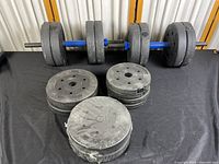 Set of two adjustable dumbbell bars with several concrete/ plastic-coated plates mounted, additional plates stacked in front on black surface.