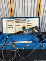Overall image of Bosch 1632VS reciprocating saw in blue metal case with blades and instruction manual inside.