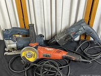 Three corded electric power tools: Bosch rotary hammer, Hilti cutoff wheel tool, Bosch jigsaw on black cloth surface