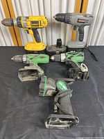 Four cordless drills from DeWalt, Craftsman, and Hitachi on black surface, showing front angle.