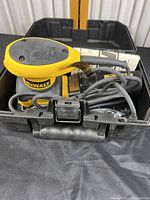 DeWalt palm sander coiled and placed inside open carrying case showing cord and dust bag attachment.