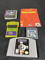 Image showing Star Wars Nintendo 64 cartridge, Japanese Pokémon Silver Game Boy Color cartridge, Sega Game Gear cartridge with clear case, yellow Mega Memory Card, and Mission Impossible booklet only.