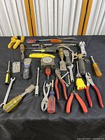 Various hand tools laid out on black cloth surface showing screwdrivers, pliers, wrenches, hammers, tape measure, and other hand tools