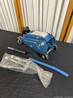Full view of the blue hydraulic floor jack with included handle and metal accessories, some parts in plastic bag.