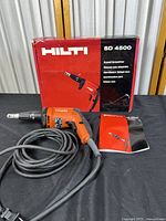 Hilti SD 4500 drywall screwdriver with box and manual on black cloth backdrop.
