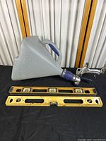 Gray Kobalt gravity fed air pressure tool with blue handle and metallic hose gun placed on black surface alongside two yellow metal levels showing paint residue and minor scratches