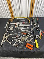 Overview photo showing the collection of assorted hand tools including wrenches, pliers, screwdrivers, box cutter and extension cord spread out on black cloth.