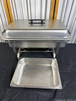 Front view of the chafer dish showing the lid with plastic handle, base frame, and fuel holder underneath, dish pan pulled forward.