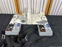 Top-down and angled view of Star Wars-themed plastic play set featuring control panels with buttons, molded terrain resembling snow and mechanical parts, and small character and vehicle figures scattered on the set.