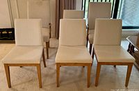 Front view of three dining chairs in a row showing light beige upholstery and oak legs.
