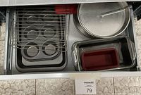 Drawer view showing three metal muffin tins with six cup molds each, a wire rack, metal loaf pans, a round metal cake pan, a rectangular glass baking dish with red silicone loaf loaf pan insert.