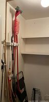 Photo showing cleaning tools with red handles including a mop, broom, and step stool/luggage cart in a storage closet